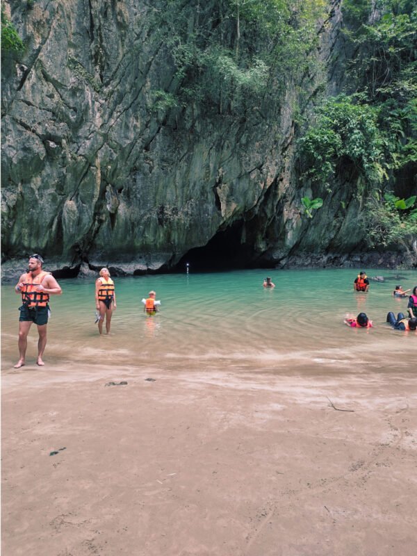 People swimming and standing in the water of Emerald Pool, admiring huge limestone cliffs inside Emerald Lagoon on Koh Mook