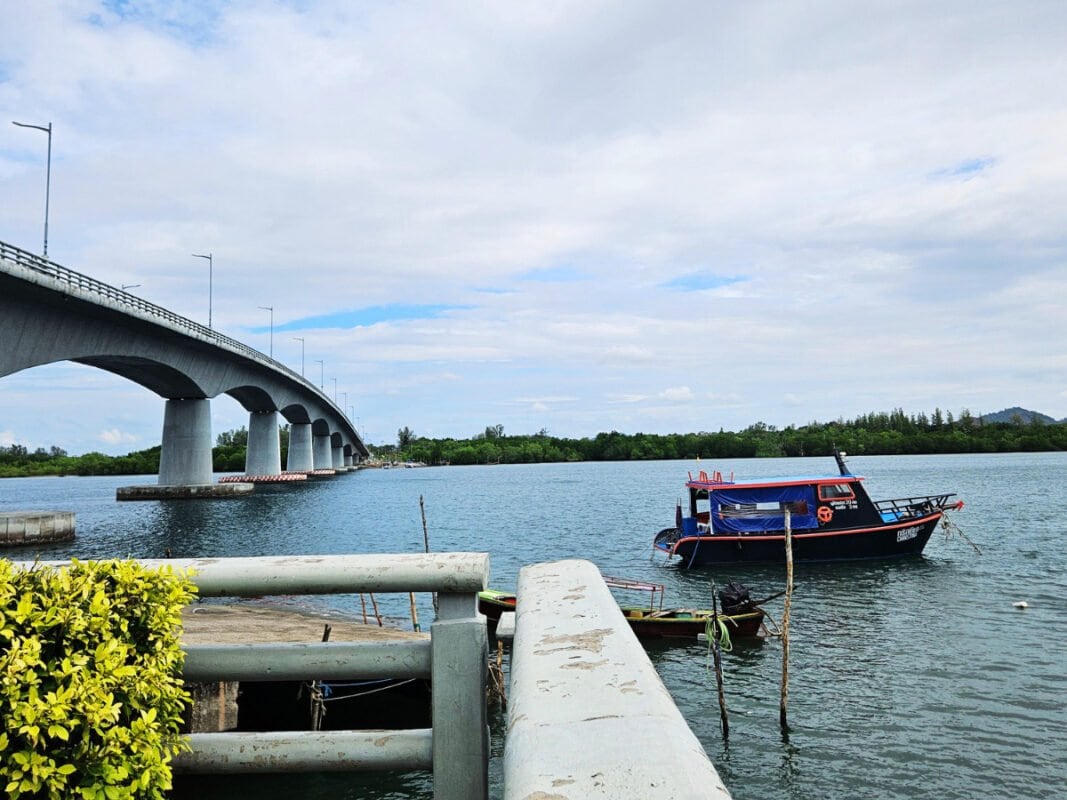 Bridge connecting the mainland to Koh Lanta in Southern Thailand with a small fishing boat on the river below.