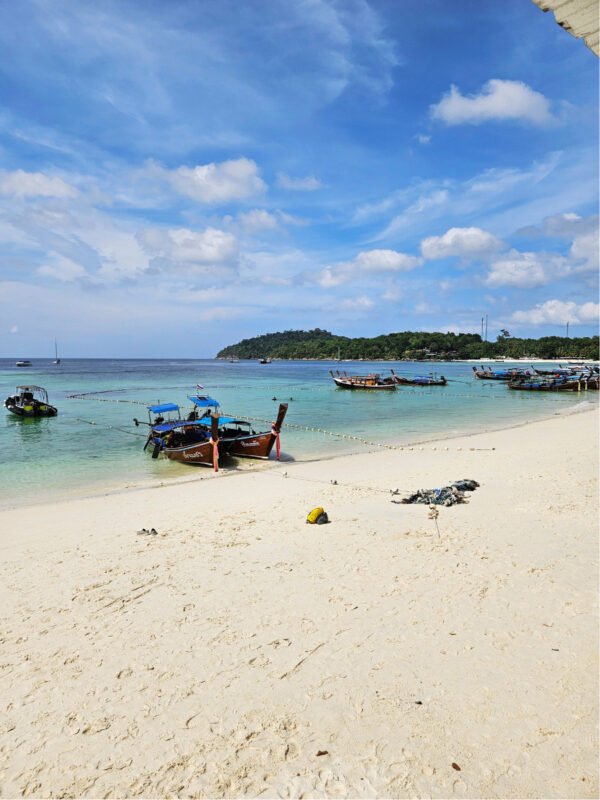 White sandy beach, and boats on Koh Lipe Pattaya beach, green hills in the horizon