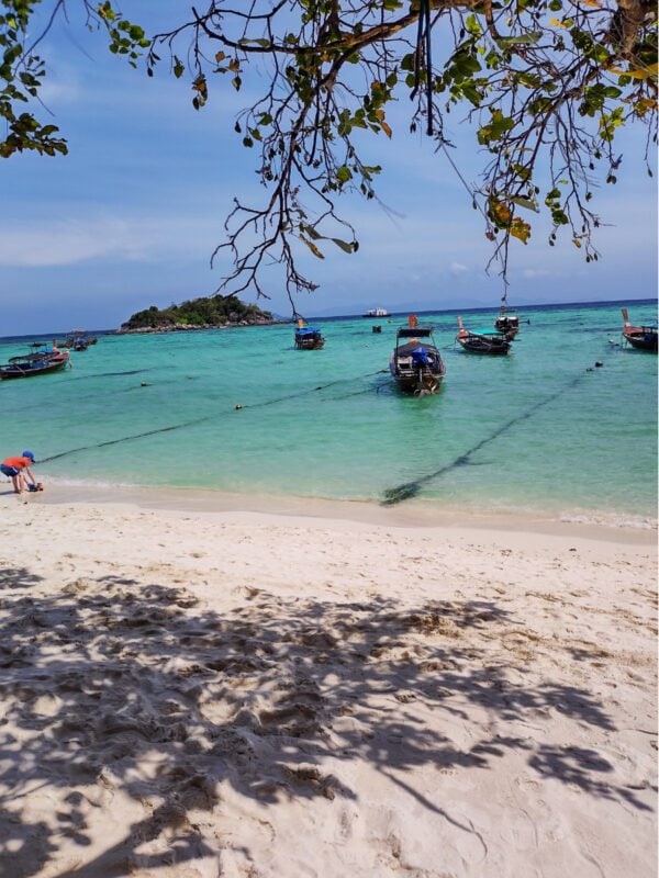 White sandy beach, and boats on Koh Lipe Sunrise beach; small, green islands in the horizon.