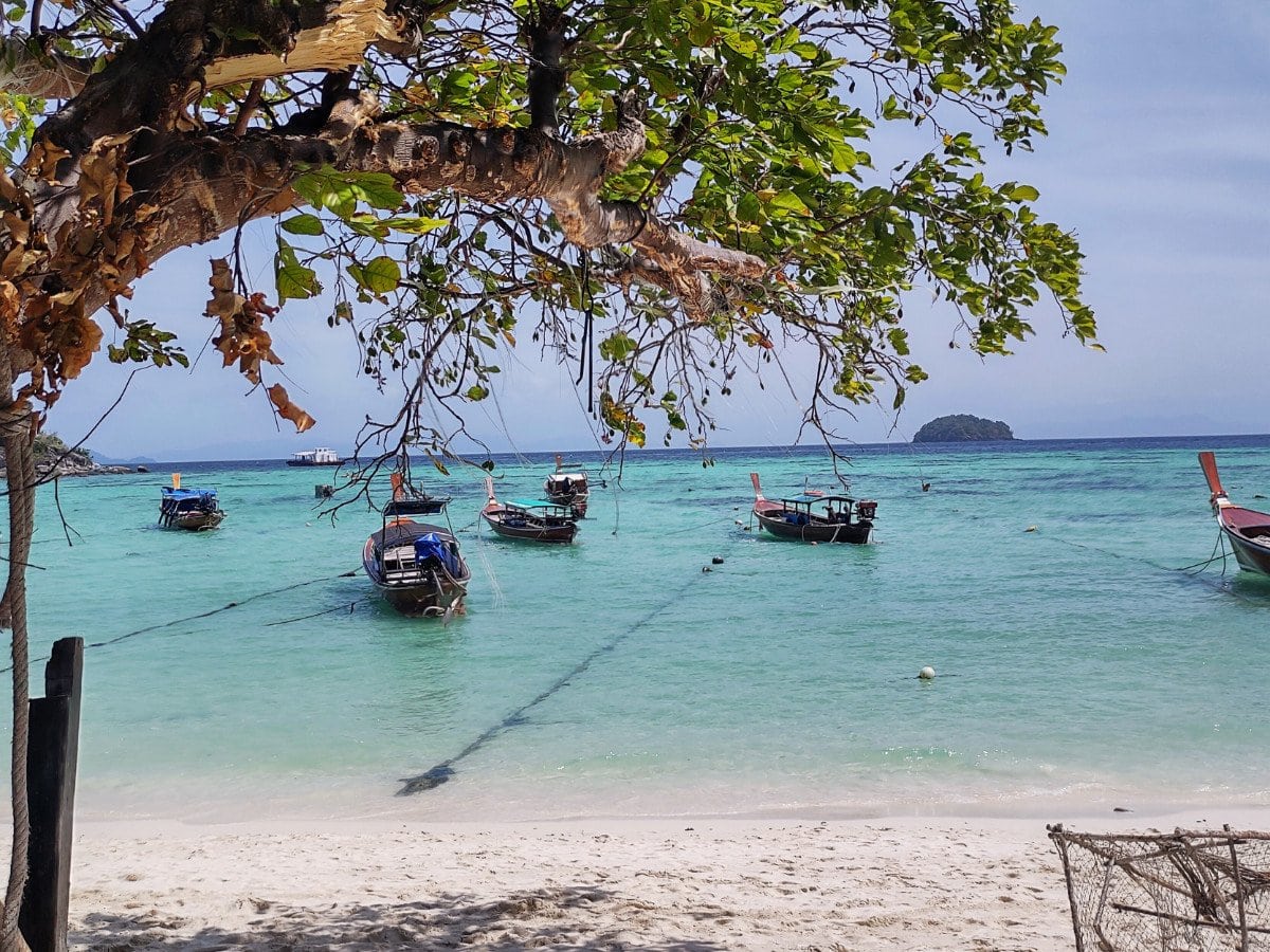 Blue clear water, boats by the beach and tree on Koh Lipe, Thailand
