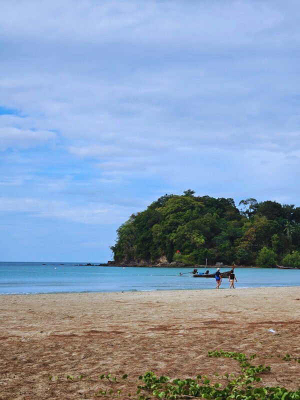 People walking on the beach, boat and jungle covered cliff, Koh Lanta