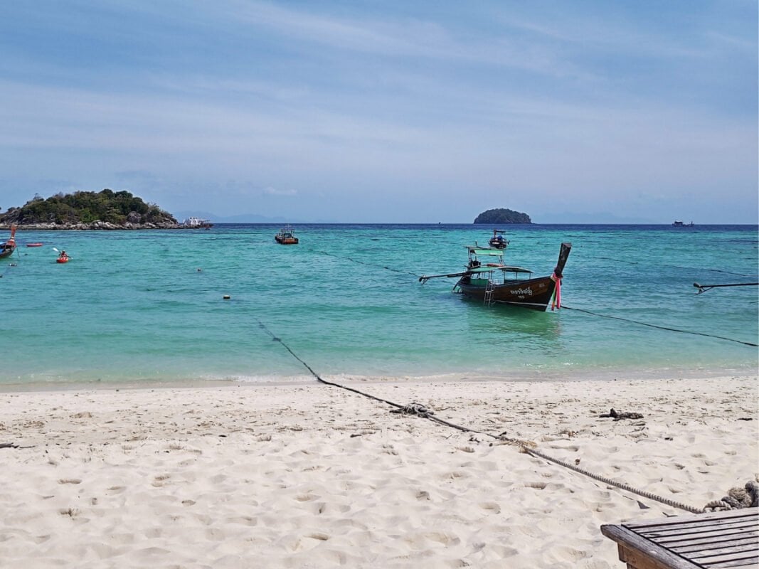 White, sandy beach, blue, turquoise water, boats and Kla island in the horizon, at the Sunrise Beach on Koh Lipe