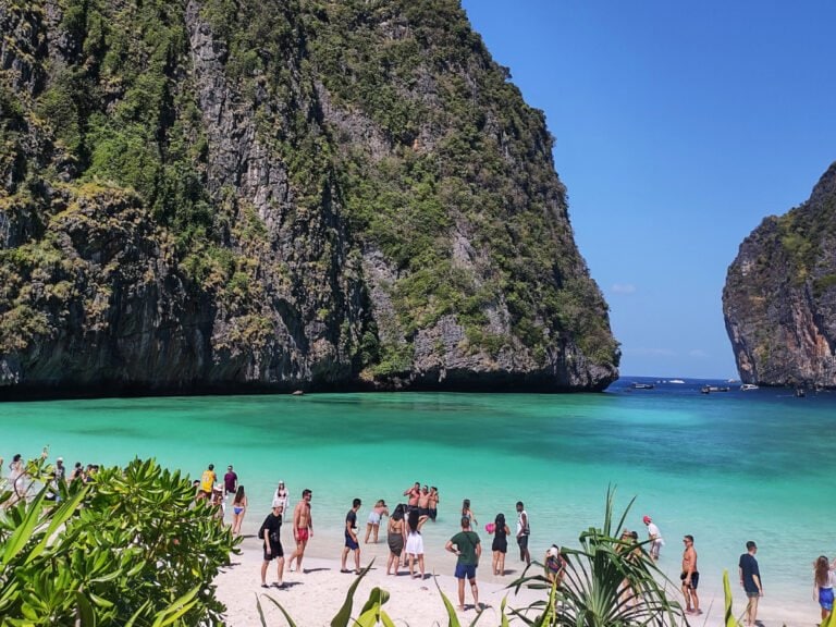 View of the Koh Phi Phi Leh Maya Bay, tourists on the beach, clear, blue sea and huge limestone cliffs in the distance