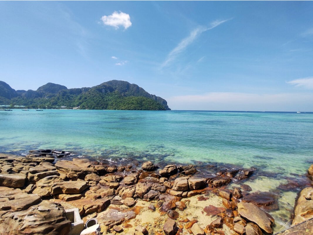 Koh Phi Phi rocky beach, clear, blue sea, mountains covered with jungle in the distance