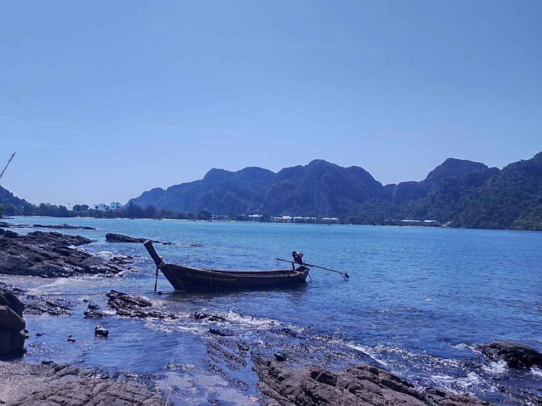 Koh Phi Phi rocky shore, fisherman boat and limestone cliffs in the distance