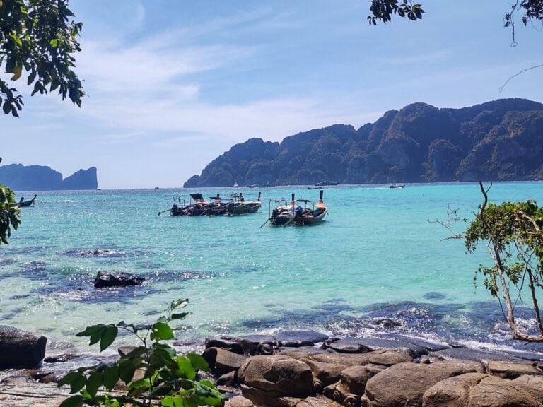 Koh Phi Phi rocky shore, big stones, boats, clear blue sea and limestone cliffs in the distance