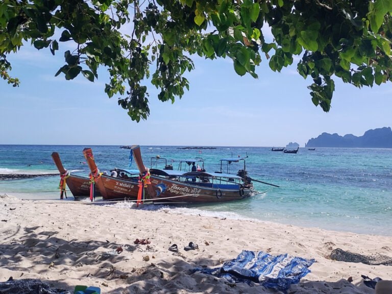 Koh Phi Phi sandy Long beach and 4 long tailed boats, blue sea and cliffs in the distance