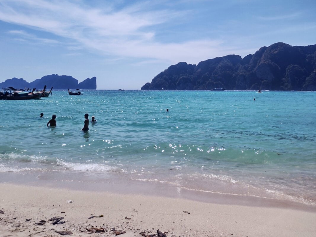 Koh Phi Phi clear blue sea, people in the water, boats and mountains in the distance