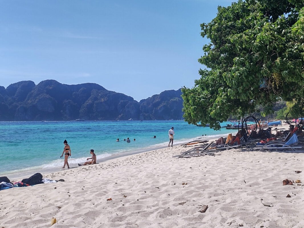 Koh Phi Phi people on a sandy beach and under the tree, and mountains in the distance