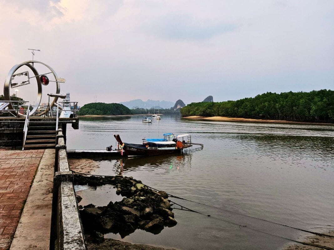 Sculpture on a promenade by Krabi river, boat and mangroves in the distance