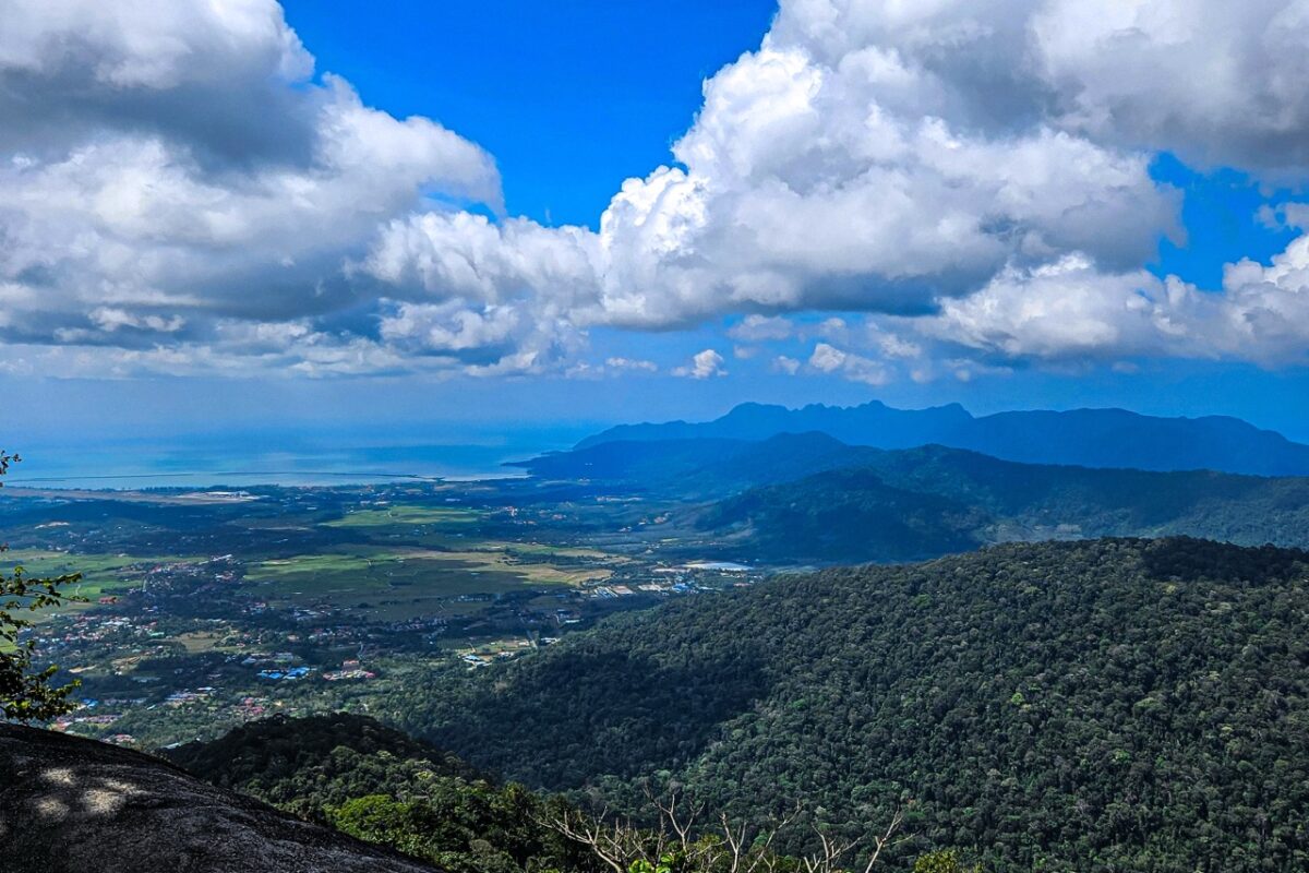 An expansive aerial view of Langkawi’s coastline and lush green valleys under dramatic white clouds.