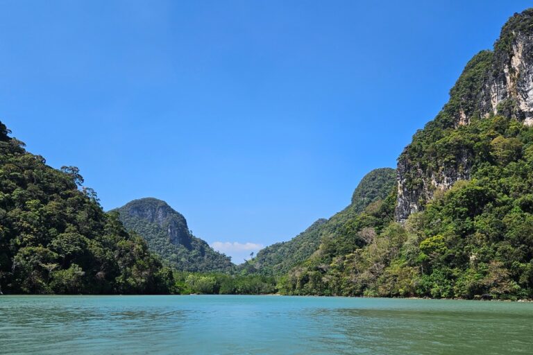 A narrow sea passage framed by steep, tree-covered limestone cliffs leading to distant hills.