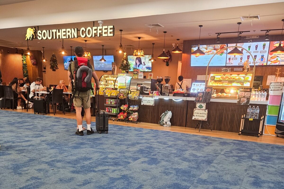 Traveler with backpack standing at a café inside Krabi International Airport terminal in Southern Thailand.