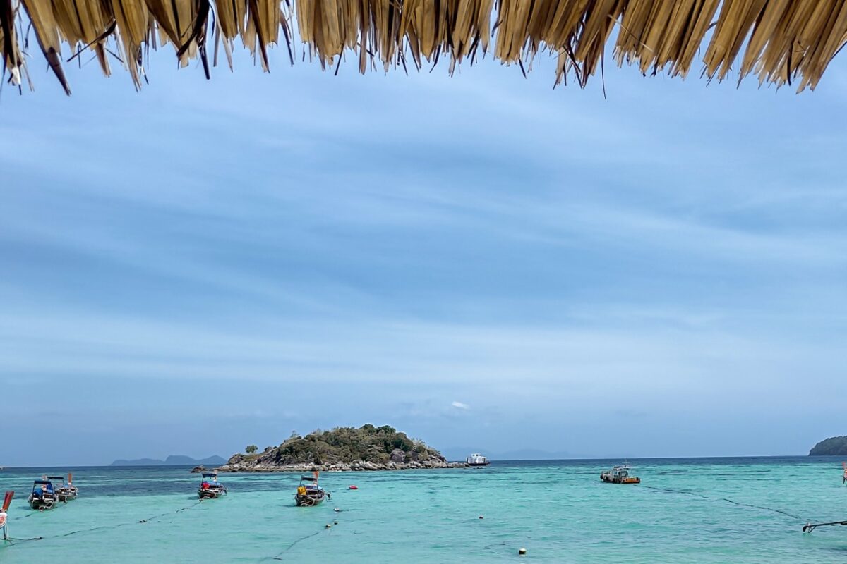 Wide view of Sunrise Beach Koh Lipe with white sand and clear shallow water and small island in the distance
