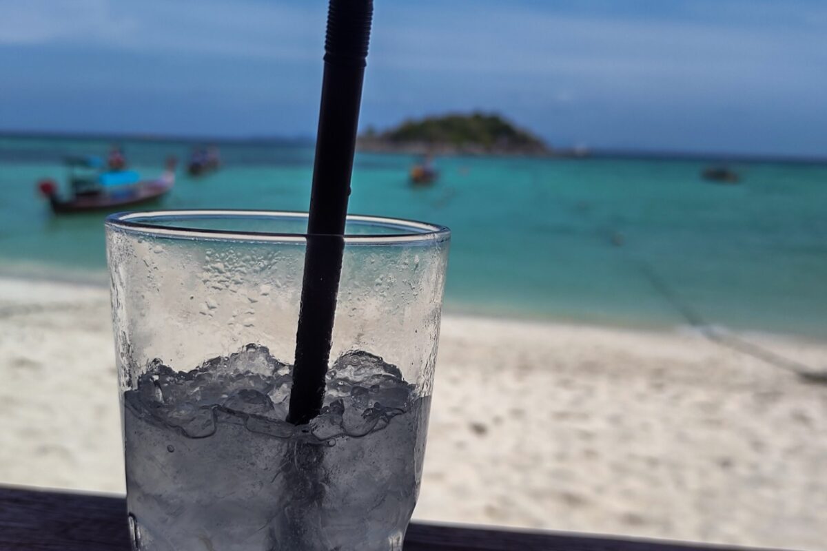 Drink with ice overlooking Sunrise Beach in Koh Lipe with turquoise sea and longtail boats, one of the best things to do in koh lipe
