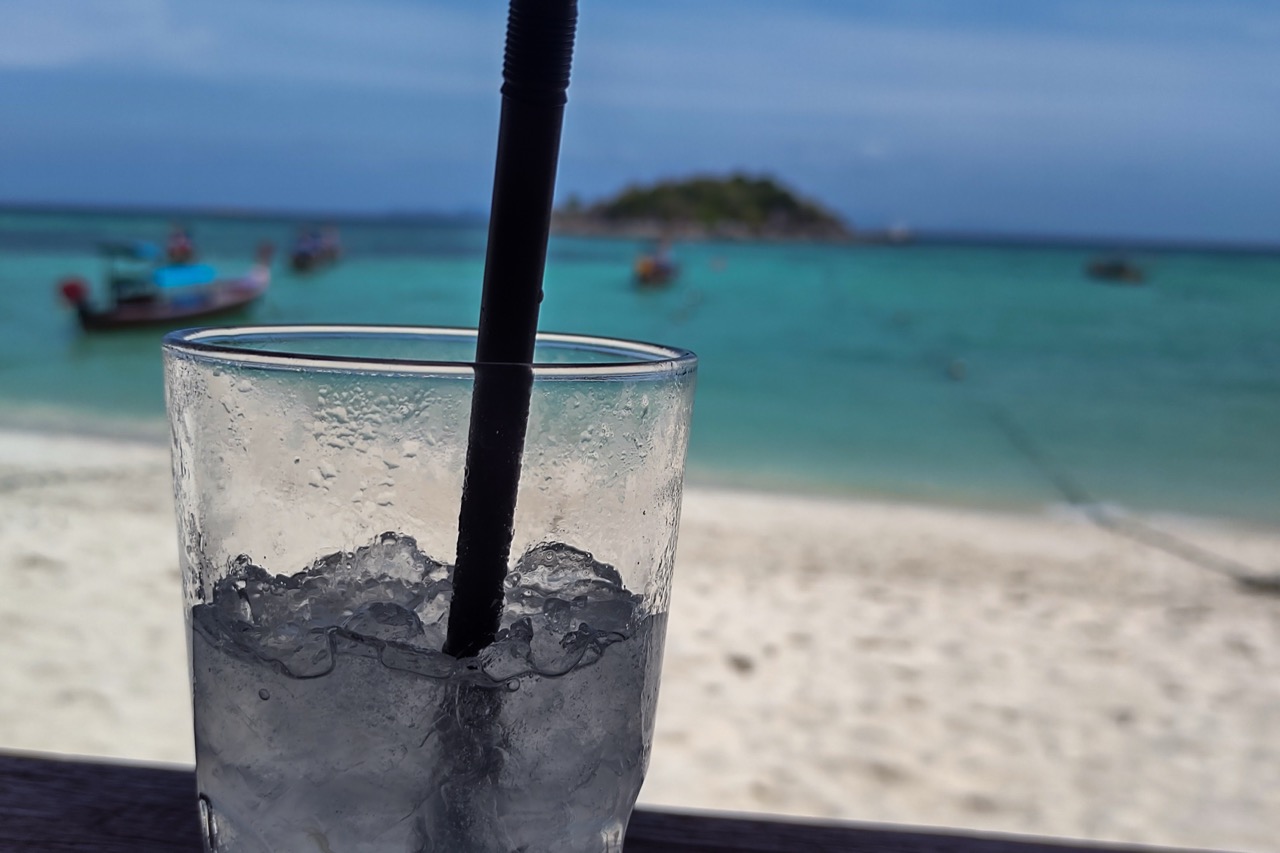 Drink with ice overlooking Sunrise Beach in Koh Lipe with turquoise sea and longtail boats