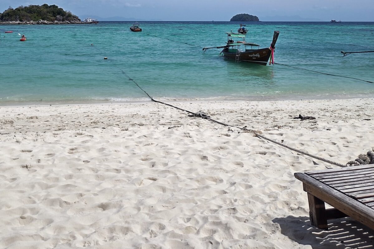 Longtail boats at Sunrise Beach Koh Lipe with calm sea and sandy shoreline, Thailand
